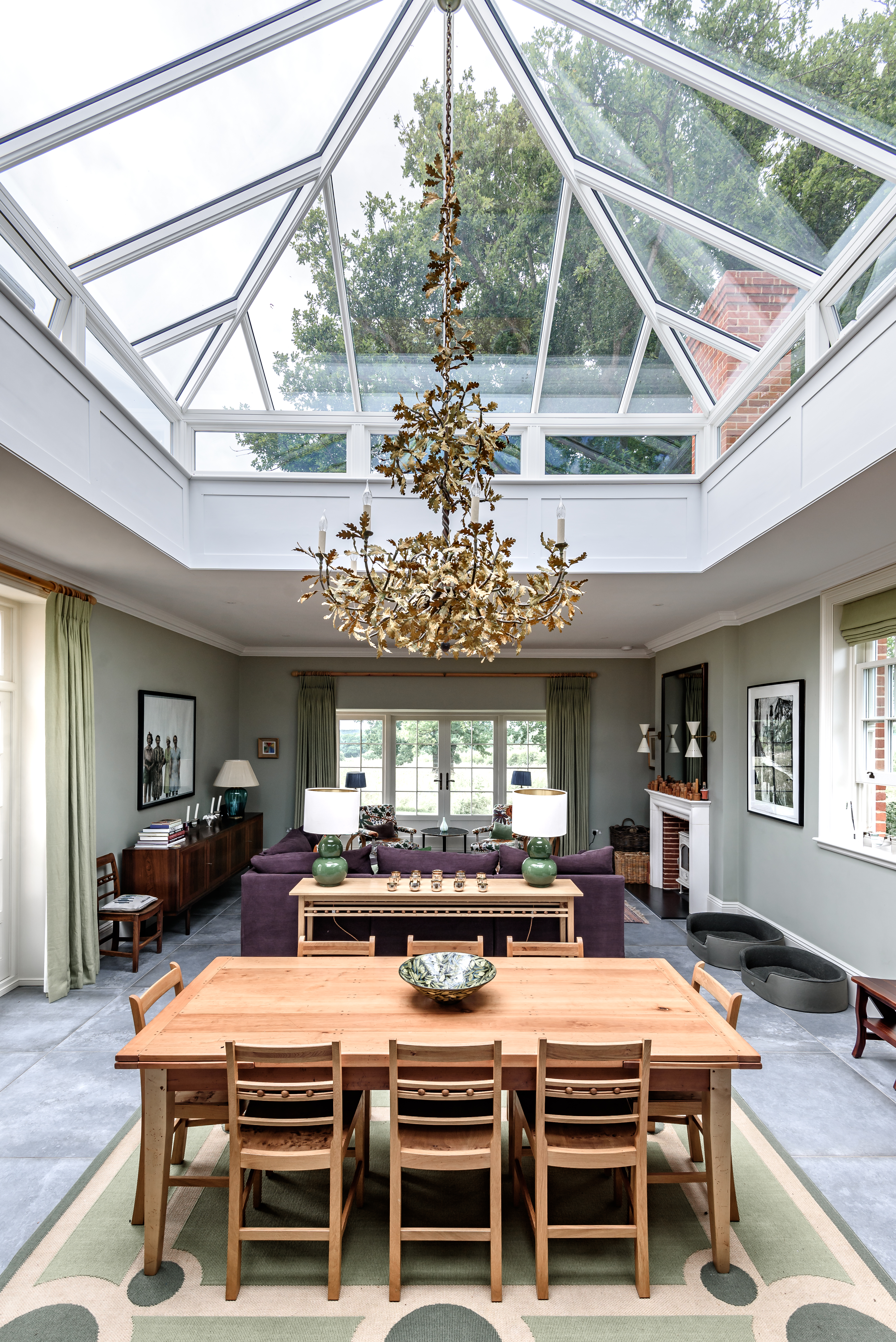 A spacious and elegant living-dining area illuminated by a stunning pyramid roof lantern with side frames, allowing abundant natural light to flood the space. A statement chandelier adds grandeur to the classic interior design.