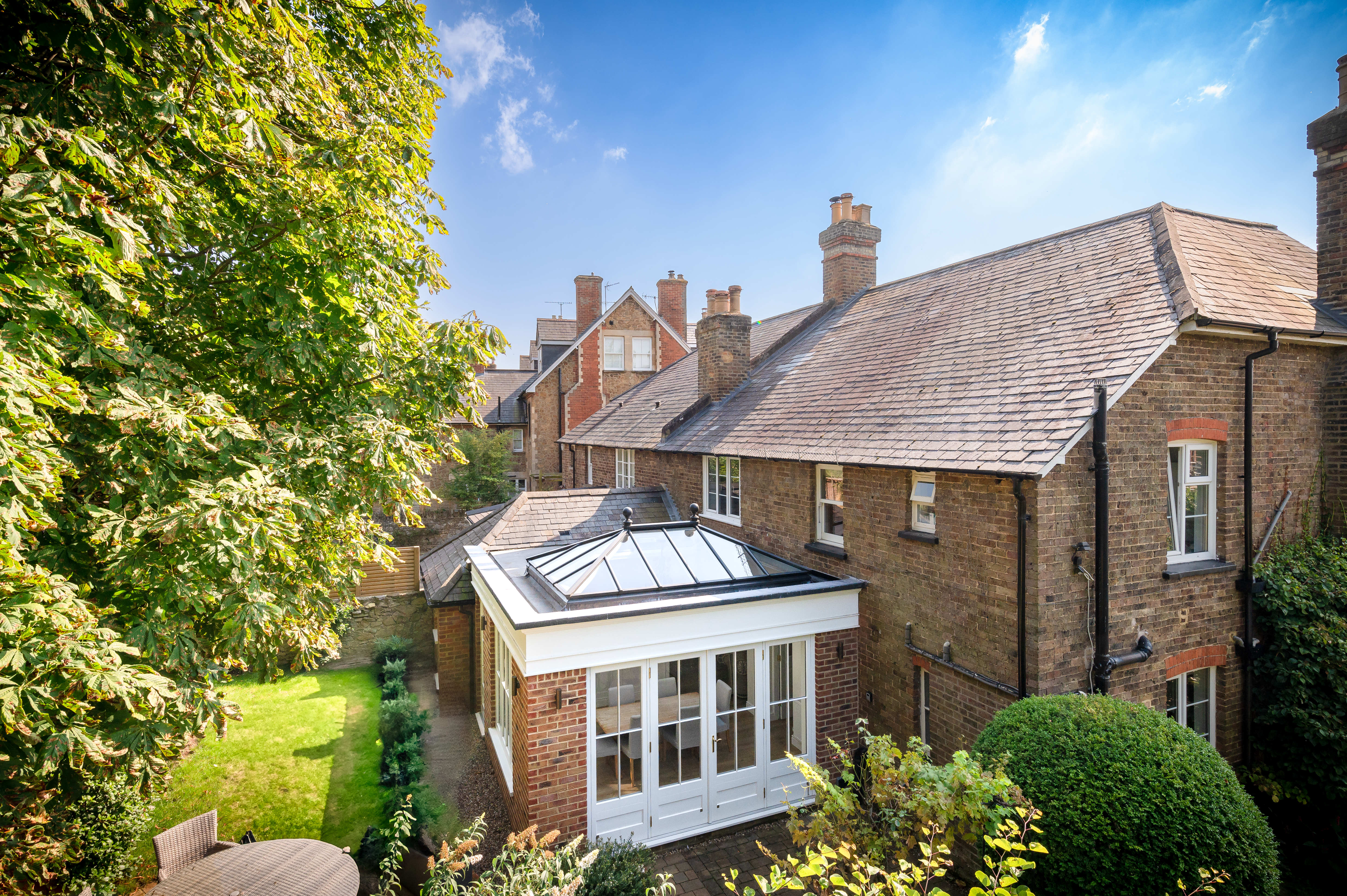 A beautifully designed orangery extension featuring a classic timber roof lantern, set within a flat roof with a parapet cornice. The structure seamlessly blends with the traditional brick home, enhancing both style and natural light.