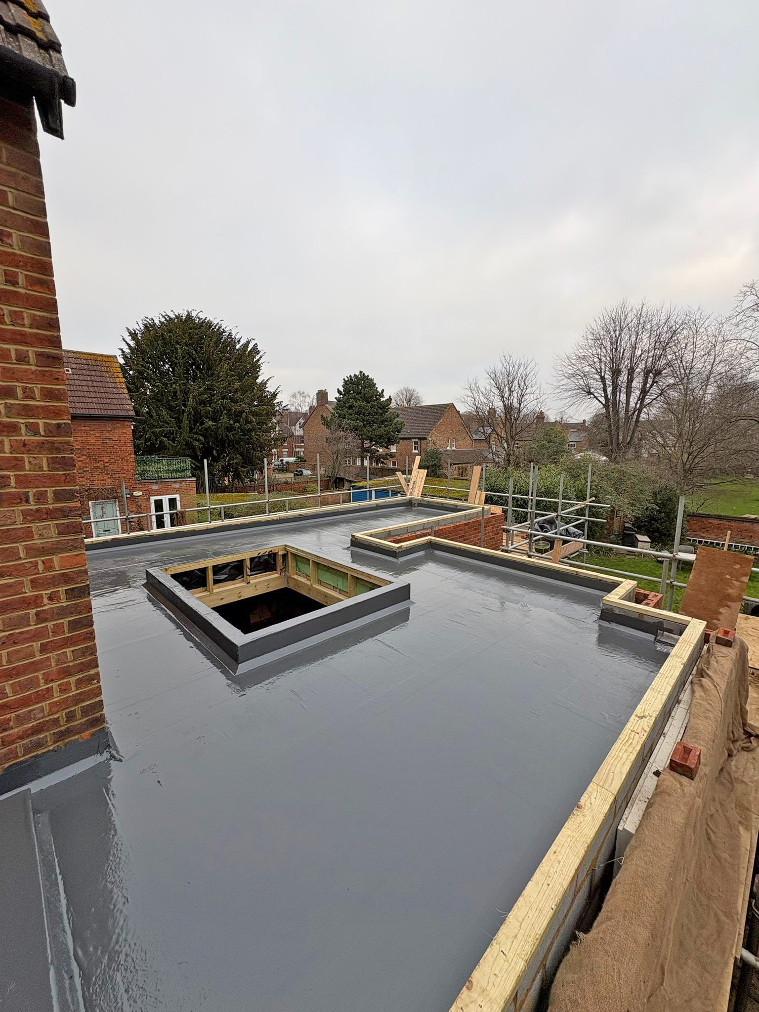 A newly installed flat roof with a smooth waterproof covering, featuring a dressed kerb prepared for a roof lantern installation. The construction site is in progress, showcasing a modern roofing solution.